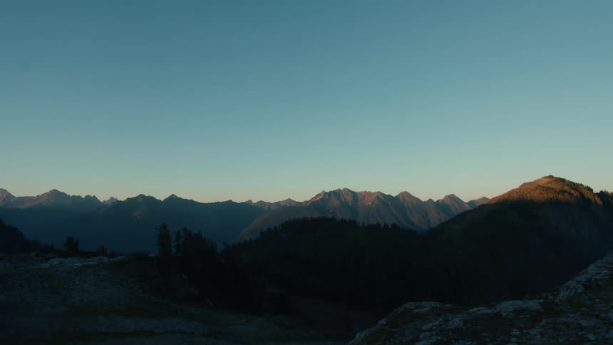 A range of mountains bathed in the warm glow of the setting sun silhouetted against a clear blue sky
