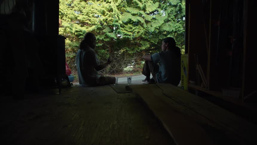 A young man and an older man are sitting in the doorway of an indoor space and are talking