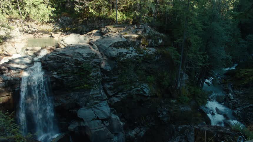 A waterfall flows down a cliff face into a shady creek