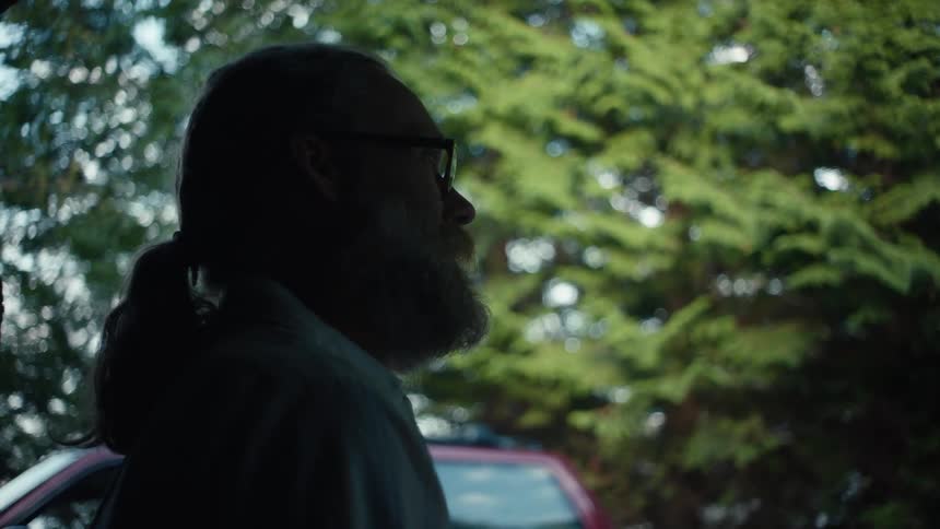A man stands outside and speaks to someone off camera