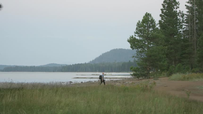 A person wearing a backpack walks a trail by the water