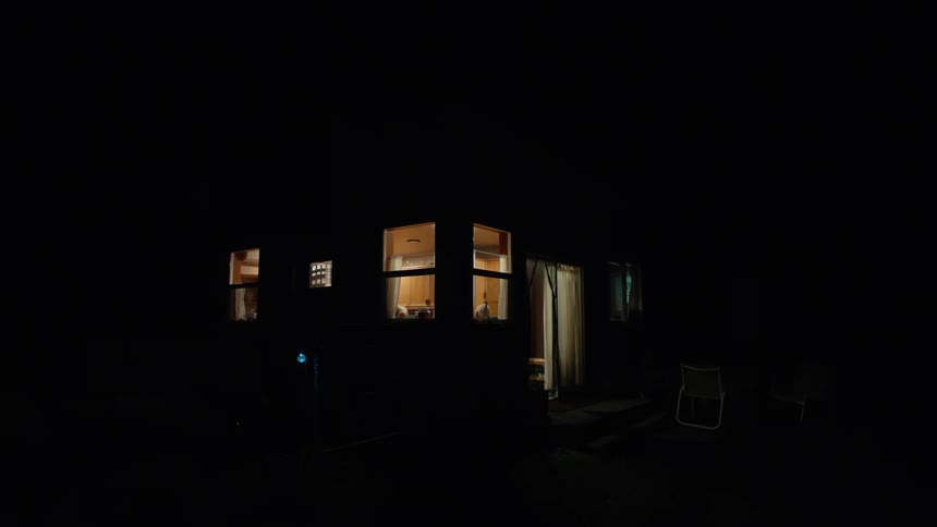 Outside view of a houses lights on at night and people walking around