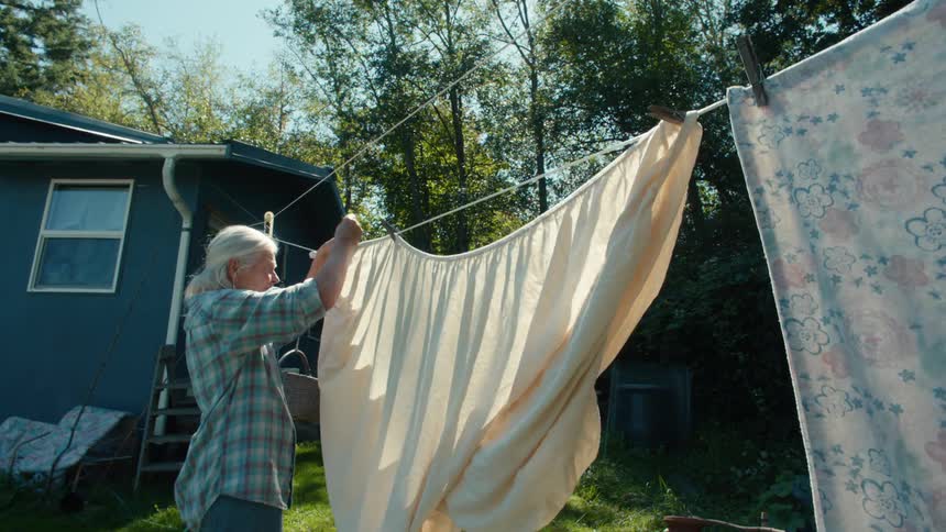 Elderly woman hanging a sheet on the clothesline in an outdoor area