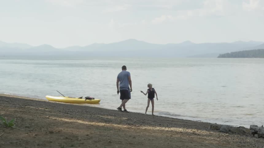 Man looking at child while child throws a rock into water
