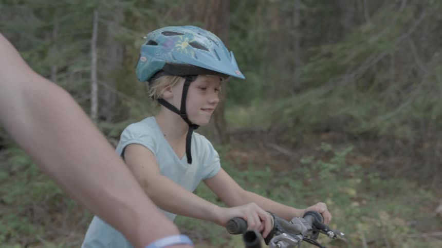 A child rides their bike with a parent in the day
