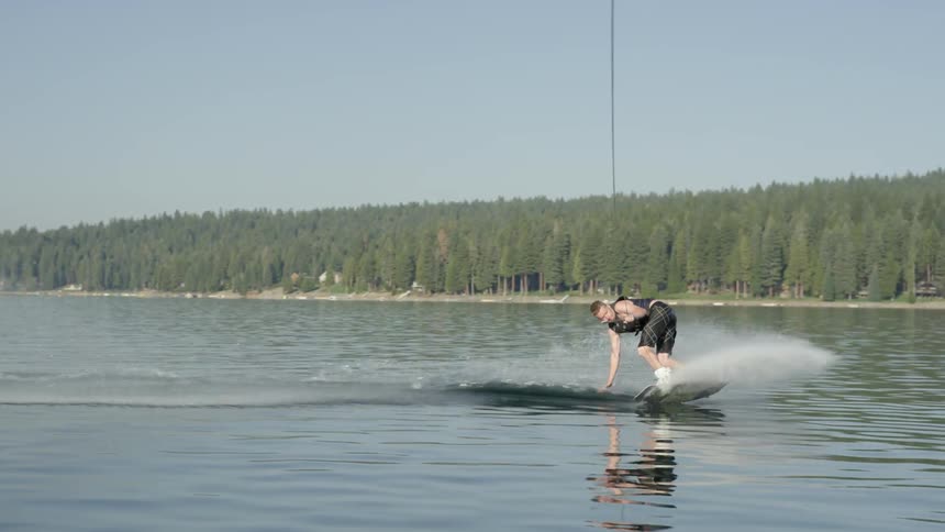 A man wake boards on a lake on a sunny day