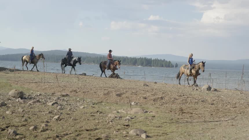 A few people riding horses on a beach or shore next to a lake