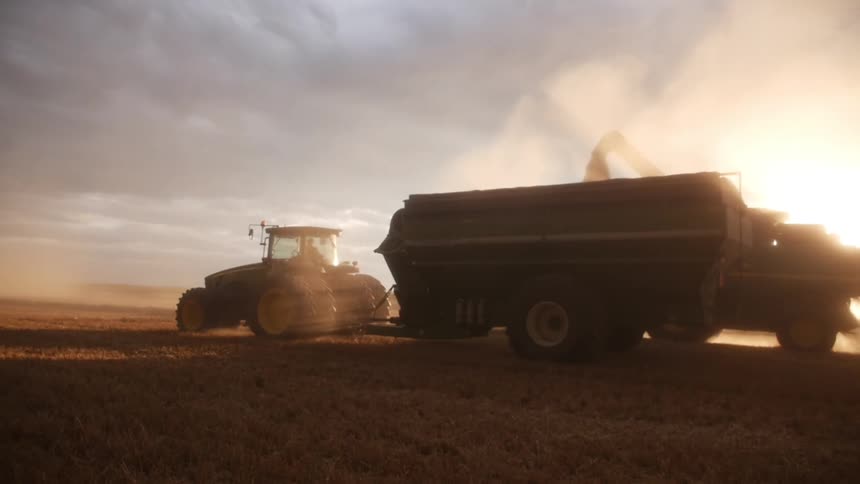 Tractor and a combine harvester in a field during sunset