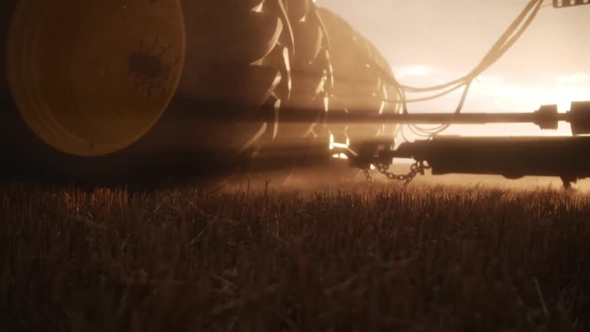 Wheels of an agricultural machine passing through a field with golden sun on the horizon