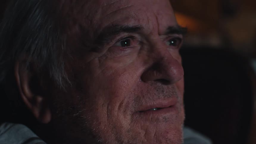 The face of an elderly man who is intently looking straight ahead while a light is flashing in his face