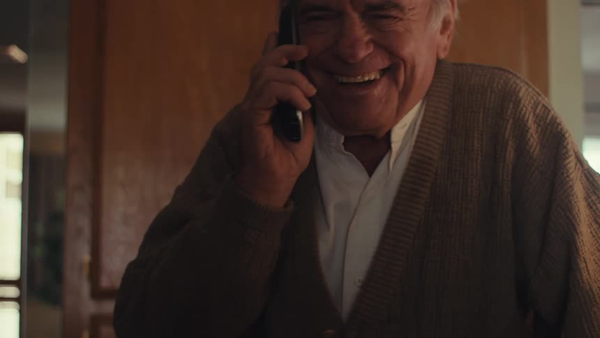 Elderly man standing and laughing while on a phone call