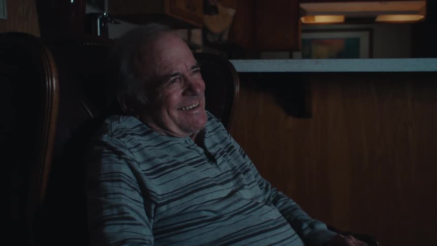 An elderly man laughing while watching television