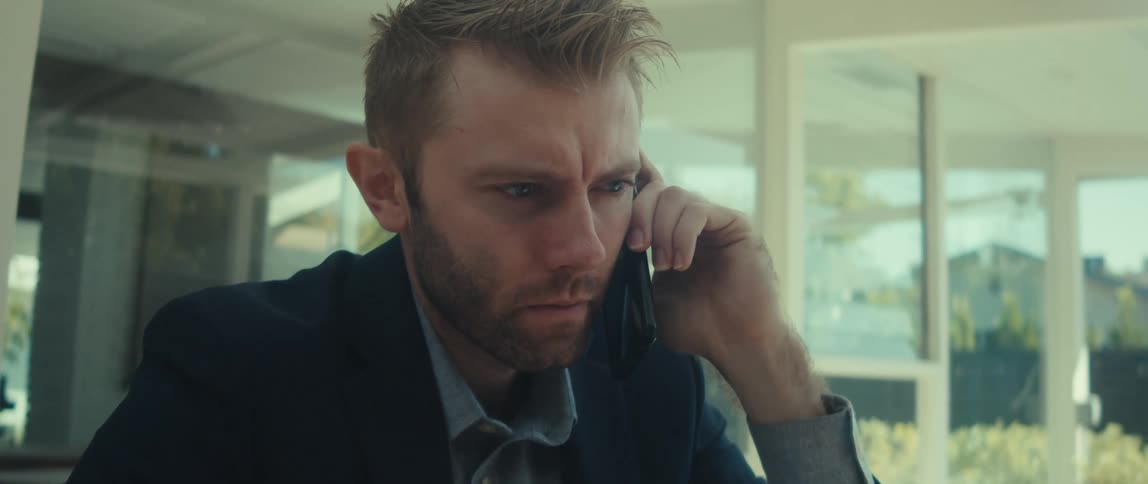 Man sitting at a table in front of an open laptop talking on his cell phone