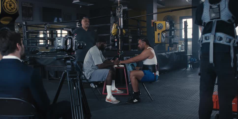 A videographer films a coach wrapping the hands of a boxer in a gym