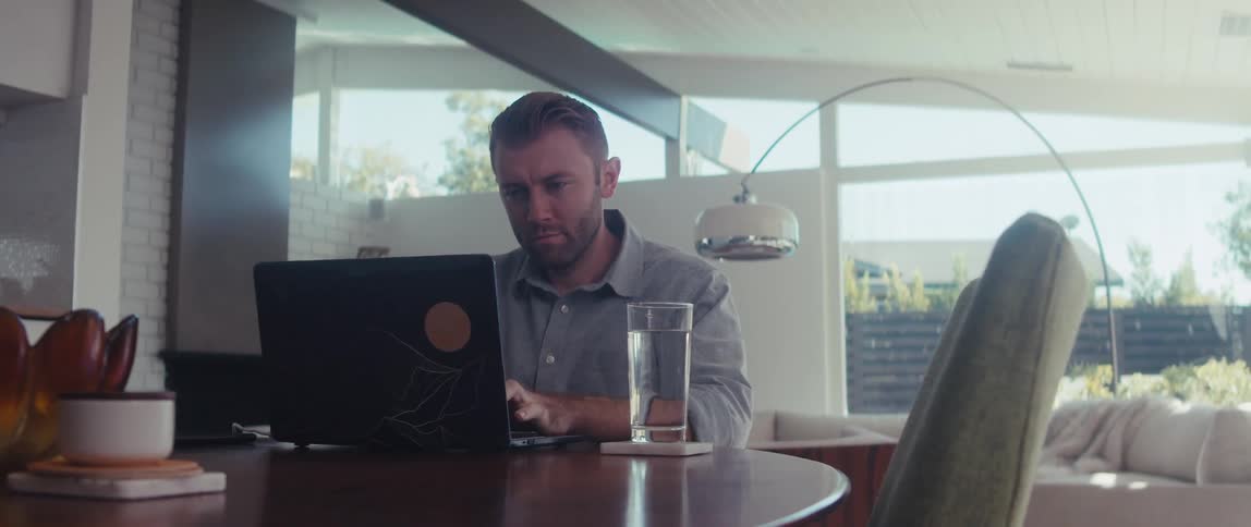 A man in a shirt works on a laptop in a welllit living room in a modern home
