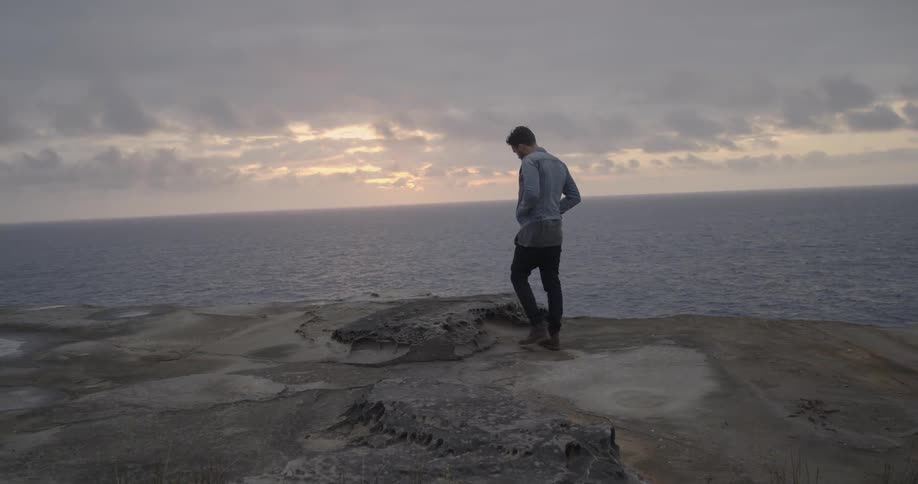 A man walks over sand to stand on a beach at dusk