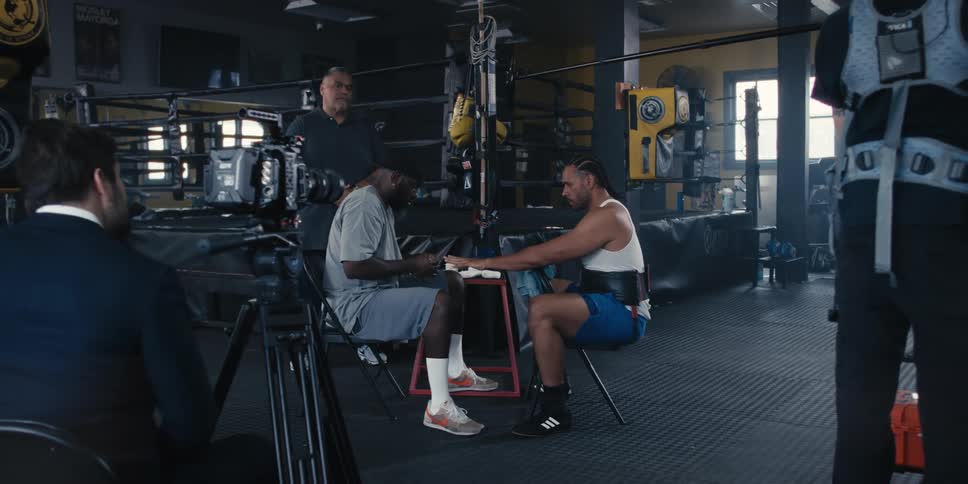 Boxing gym environment with a man putting a white belt on a fighters hands