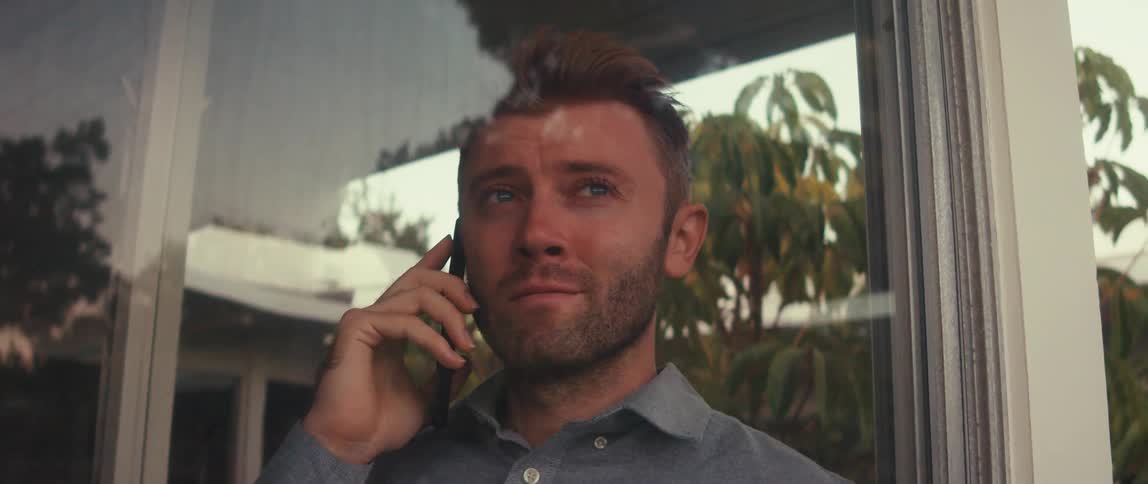 Man standing at window talking on a phone call