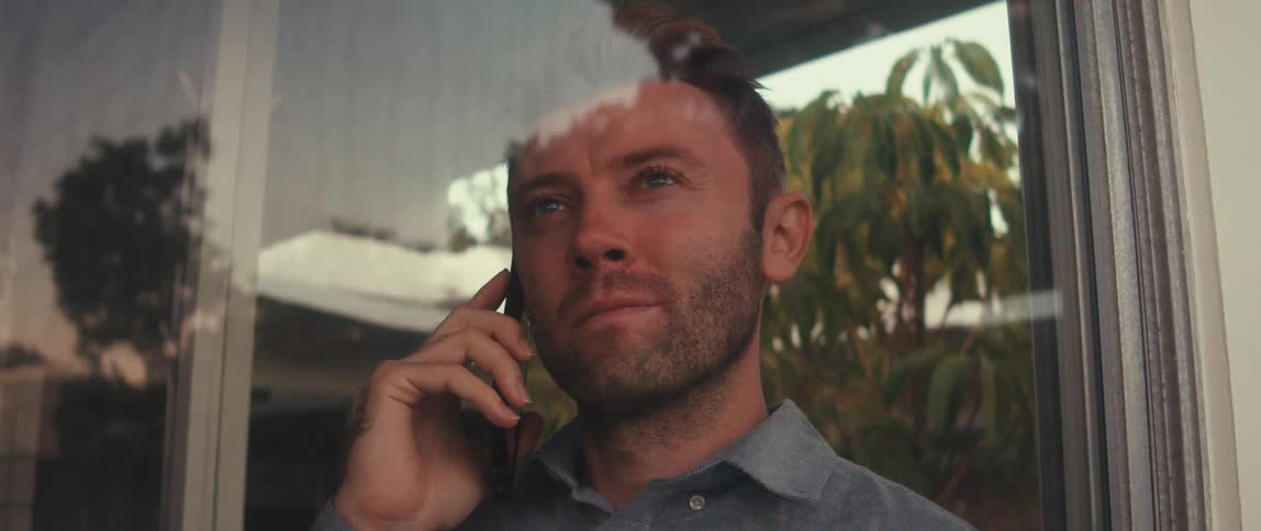 Man gazes through a window while talking on his phone