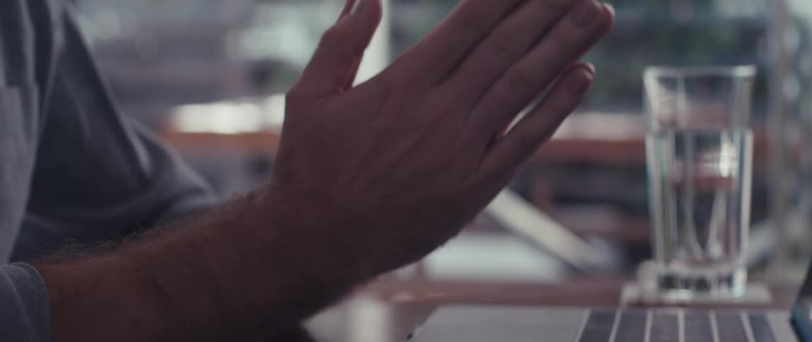 A man with his hands together moving them in front of his laptop