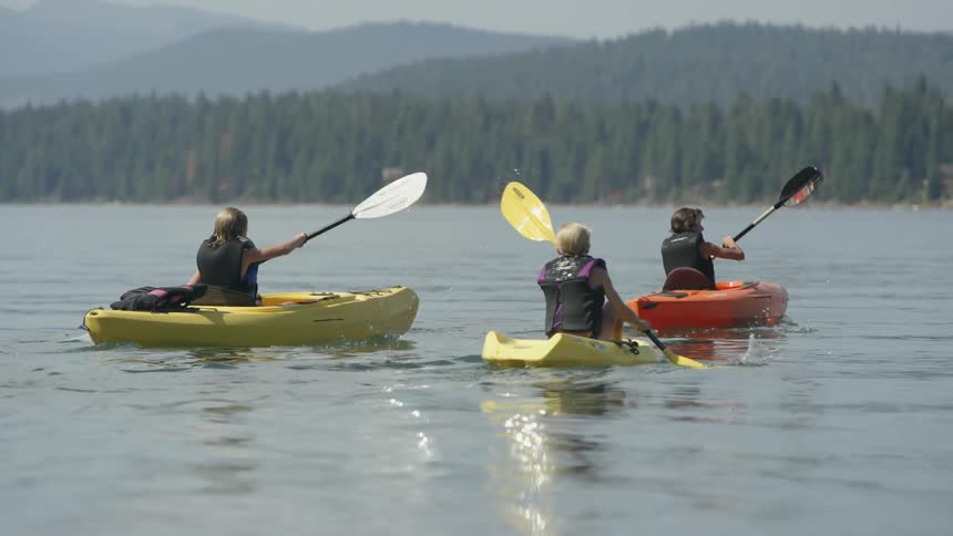 Three people paddle kayaks in a tree lined lake