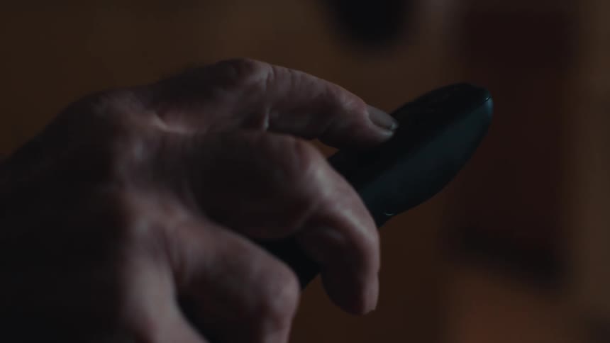 An elderly hand presses a button on a remote control