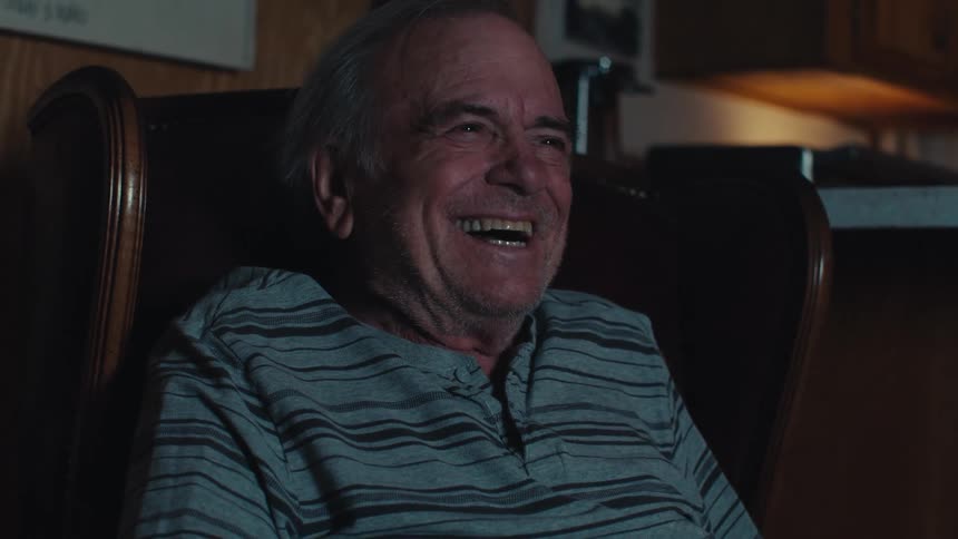 Elderly man sitting in a chair laughing out loud