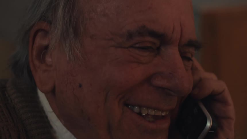 An elderly man laughing while talking on the phone