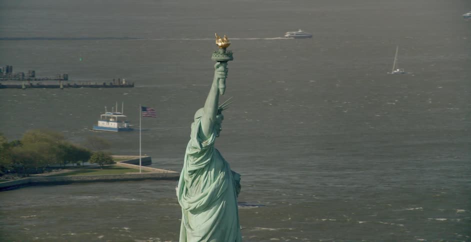 The statue of liberty with buildings and water with boats all around