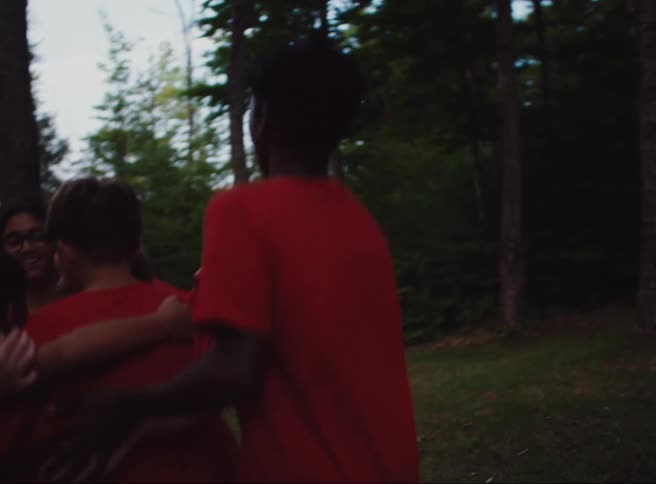 A group of children in red shirts are playing and hugging each other in a circle in a wooded area