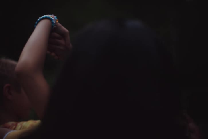 A group of people hold hands on a grassy plain near a forest
