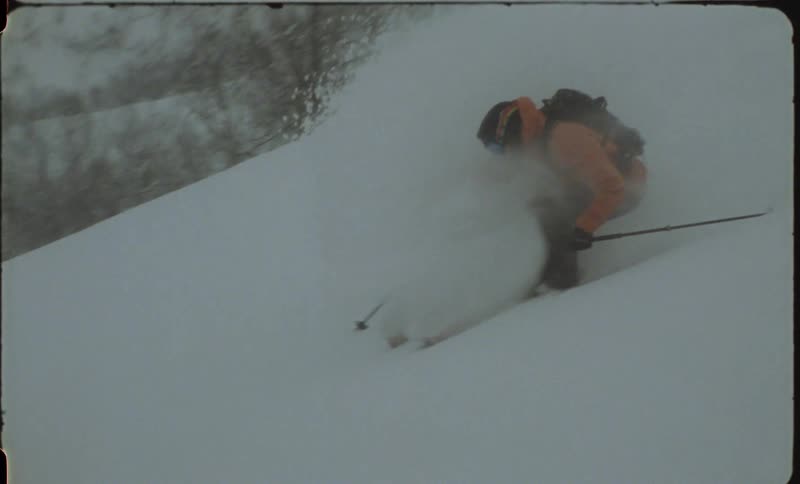 Person skiing down a snowy mountain casting snow behind them