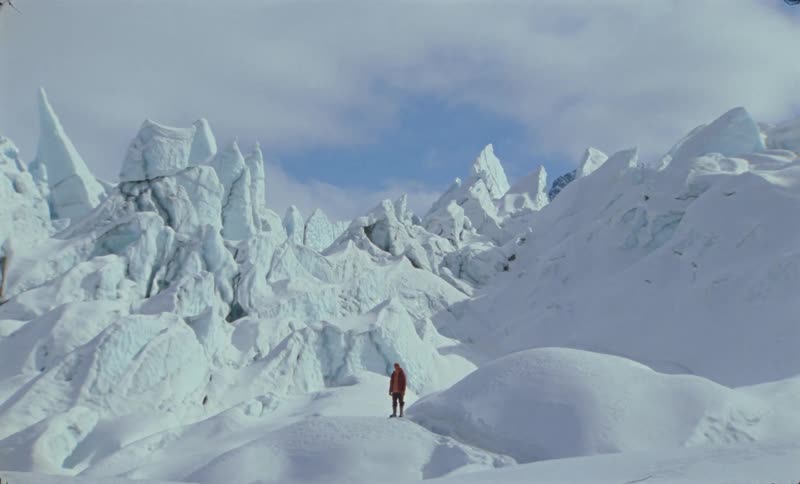 A wide clip of a person standing at the peak of an ice mountain