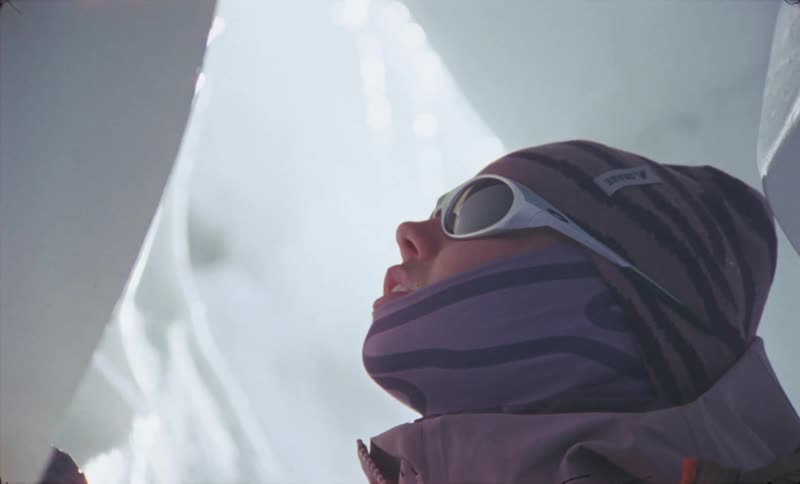 The face of a person wearing glasses and warm clothes who is between two walls of ice with small drops coming out of a stalactite