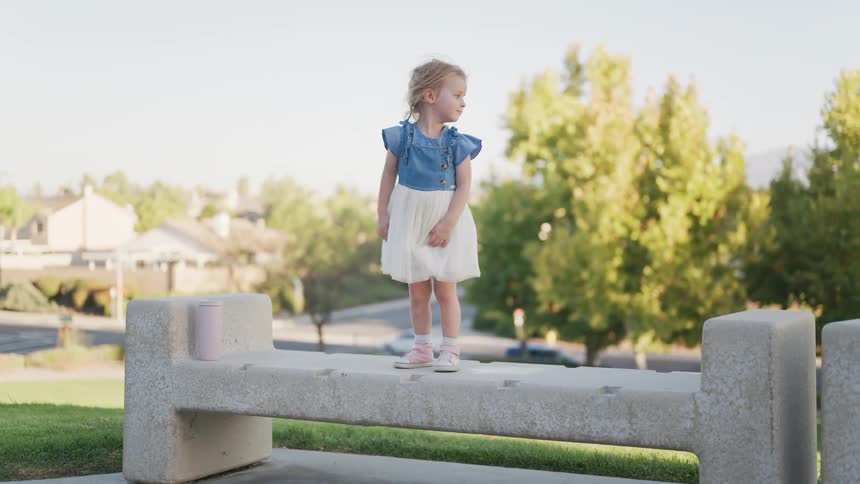 Toddler girl walks across a stone bench overlooking a neighborhood