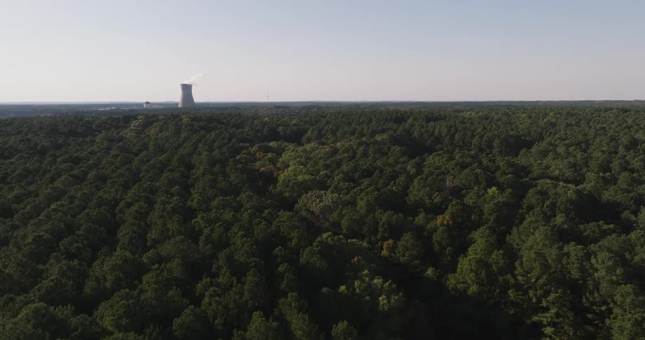 Aerial view of a dense forest with a smoke stack on the horizon from a meth factory