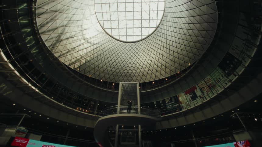 A man in a suit stands on an elevated platform inside of a cavernous structure with a large skylight in the ceiling