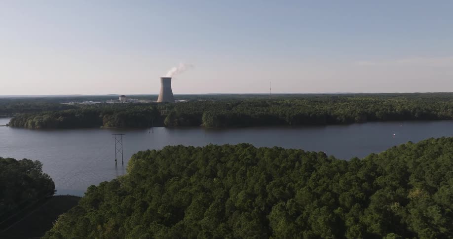 Boats float on a river as a nuclear power cooling tower emits steam in the middle of a large forest