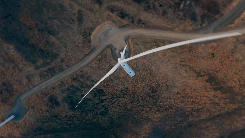 An aerial view of an event windmill with rotating propellers on a land area with a small road