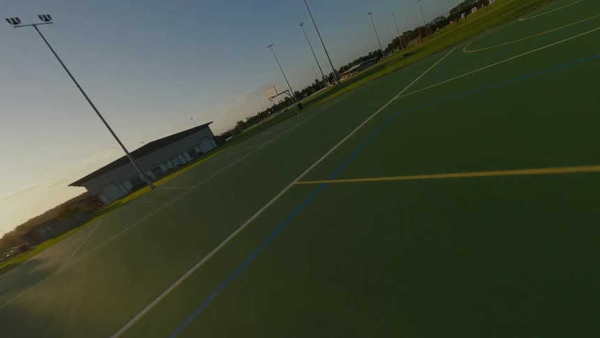 An aerial shot at sunset shows a multi purpose sports court at sunset with a building and surrounding green space visible in the background