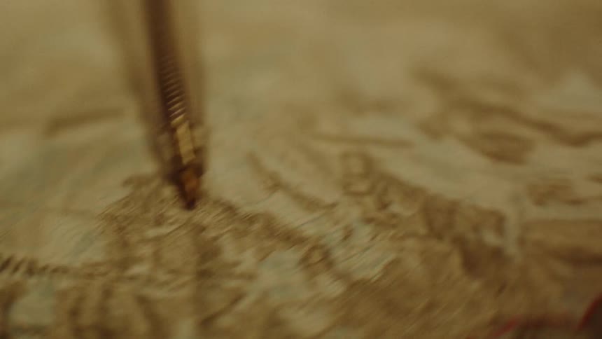 A pen pointing to a paper map with various geographical drawings and texts
