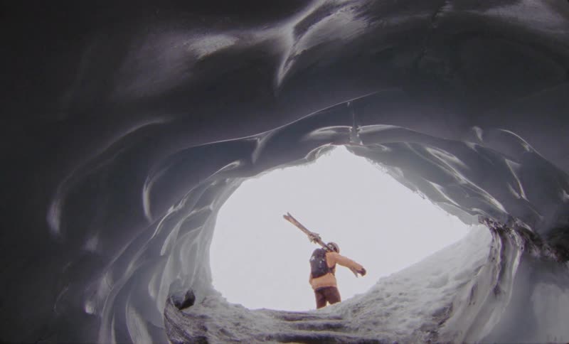 View of an ice cave from a person walking with snowboarding equipment