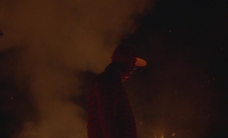 Side view of a man in a cap in a place with fire flames at night