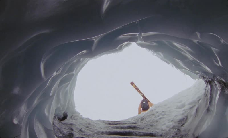 View of an ice hole and in the background a person walking with ski equipment