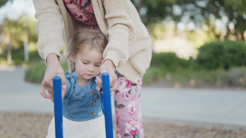 Little girl accompanied by an adult playing in a public playground