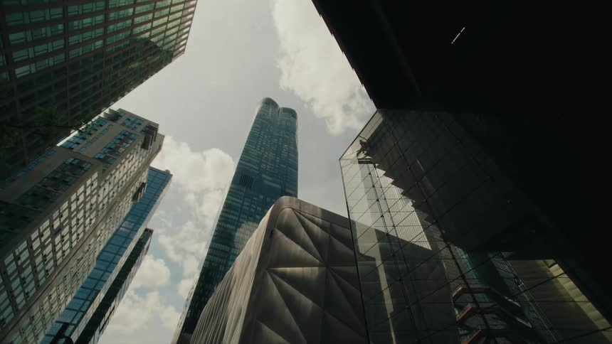 A lowangle view of towering city buildings against a bright sky