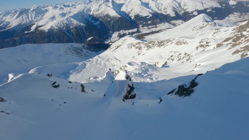 Hikers stand at the top of a slope in snowy mountainous terrain on a sunny winter day in Switzerland