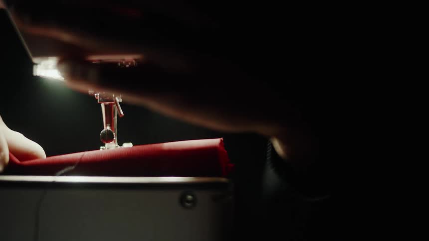 A persons hand putting red fabric into a sewing machine and then lowering the needle