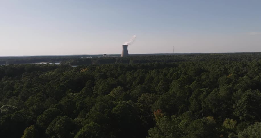 Aerial view of a dense forest and a factory with a large chimney emitting pollutants in the background