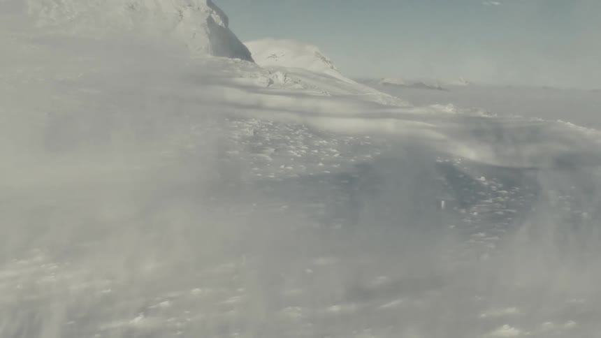 The shadow of a helicopter is cast on a snow covered mountainside as a snowdrift occurs